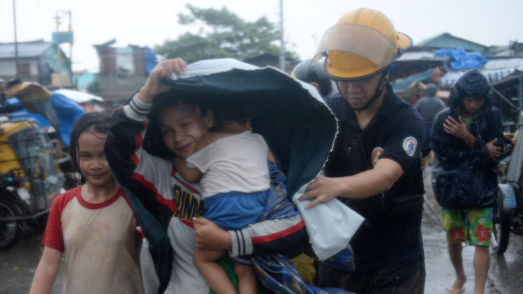 A fireman (R) helps a mother and her child evacuate from their house at an informal settlers&#39; area as Typhoon Rammasun barrels across Manila on July 16, 2014